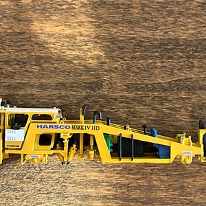 May include: A yellow and black toy construction vehicle with the text "HARSCO MARK IV HD" on the side.