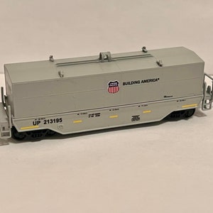 May include: A gray model train car with the words "Building America" and "UP 213195" printed on the side. The car has a black undercarriage and wheels.