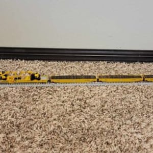 Pode incluir: Um conjunto de trem de brinquedo amarelo com vários vagões e um guindaste. O trem está em um trilho e em um tapete marrom.