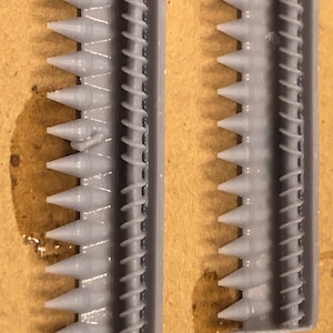 May include: Two gray plastic pieces with a series of pointed teeth on one side and a spiral pattern on the other side.