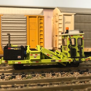 May include: A lime green CSX railroad maintenance vehicle with a black engine and a white cab. The vehicle has a yellow warning light on top and a white stripe on the side.