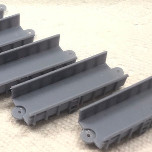 May include: Five gray plastic track pieces for a model train set. The pieces are all the same size and shape, and they have a slightly textured surface.