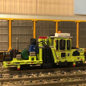 May include: A yellow and black model railroad car with a white cab and a red light on top. The car has a black and white sign that reads "ETTXX 691".