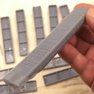 Op de afbeelding: Een set grijze plastic bouwstenen met een getextureerd oppervlak. De blokken zijn rechthoekig en hebben een reeks kleine gaten langs de bovenrand.
