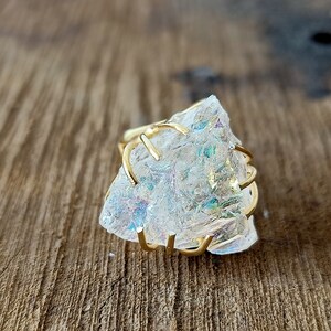 May include: A gold wire ring with a large, clear iridescent crystal. The crystal has a rough, natural texture.