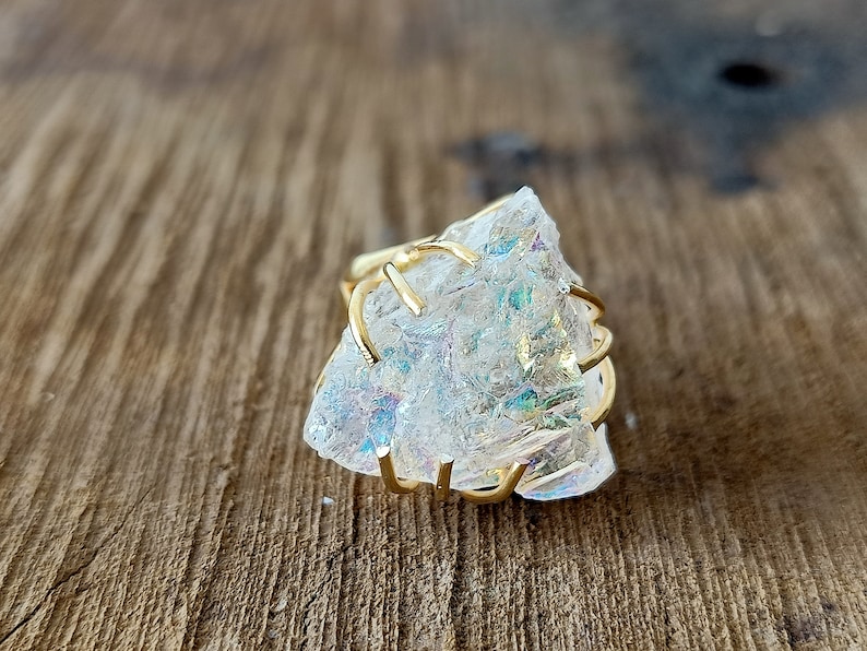 May include: A gold wire ring with a large, clear iridescent crystal. The crystal has a rough, natural texture.