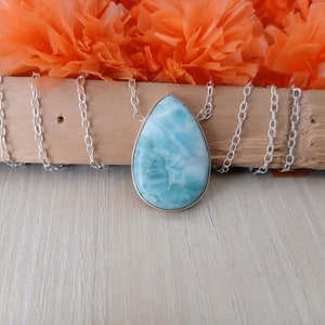 May include: A silver chain necklace with a teardrop-shaped pendant made of blue and white iridescent gemstone.
