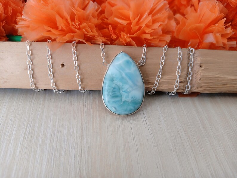 May include: A silver chain necklace with a teardrop-shaped pendant made of blue and white iridescent gemstone.