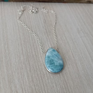 May include: A silver chain necklace with a teardrop-shaped blue and white gemstone pendant.