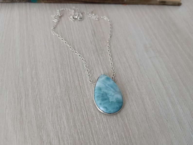 May include: A silver chain necklace with a teardrop-shaped blue and white gemstone pendant.