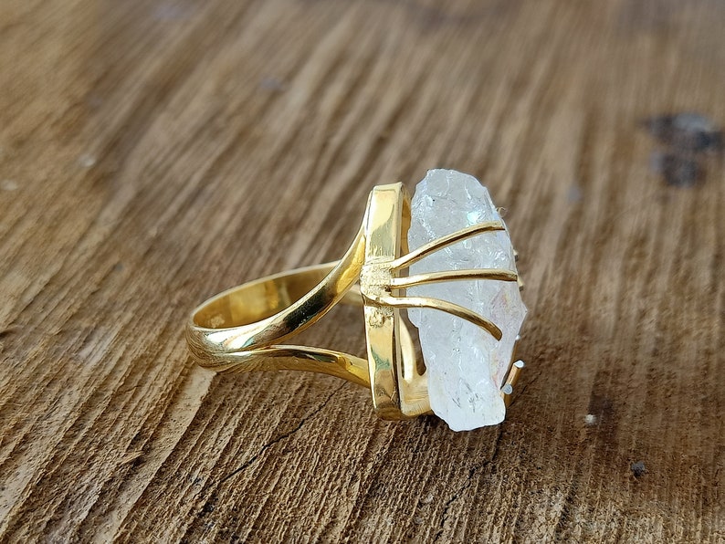 May include: A gold ring with a clear quartz crystal set in a gold cage. The ring is on a wooden surface.