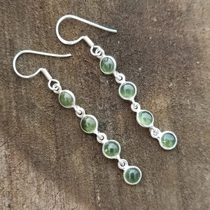 May include: A pair of silver dangle earrings with six green gemstone beads on each earring.