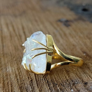 May include: A gold ring with a large, clear, iridescent crystal set in the center. The crystal is held in place by a gold wire frame.