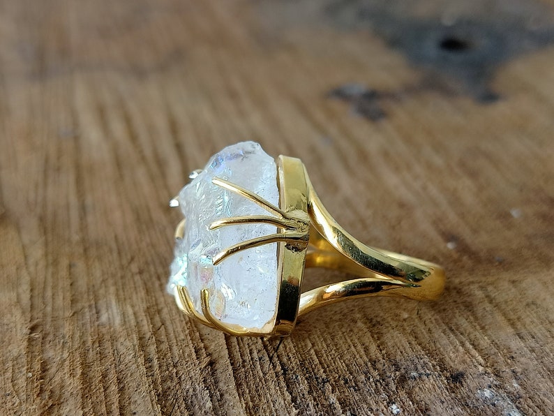 May include: A gold ring with a large, clear, iridescent crystal set in the center. The crystal is held in place by a gold wire frame.