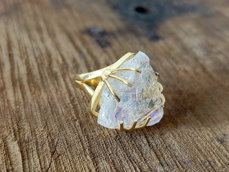 May include: A gold ring with a large, clear quartz crystal set in a cage-like design. The crystal has a slight iridescent sheen.