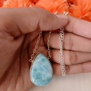 May include: A silver chain necklace with a teardrop-shaped blue and white gemstone pendant.