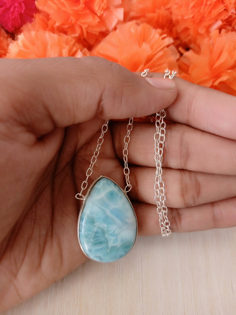 May include: A silver chain necklace with a teardrop-shaped blue and white gemstone pendant.