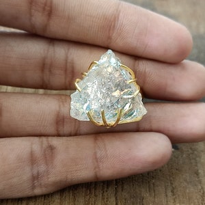 May include: A clear quartz crystal ring with a gold wire wrap. The crystal is a triangular shape and has a iridescent sheen.
