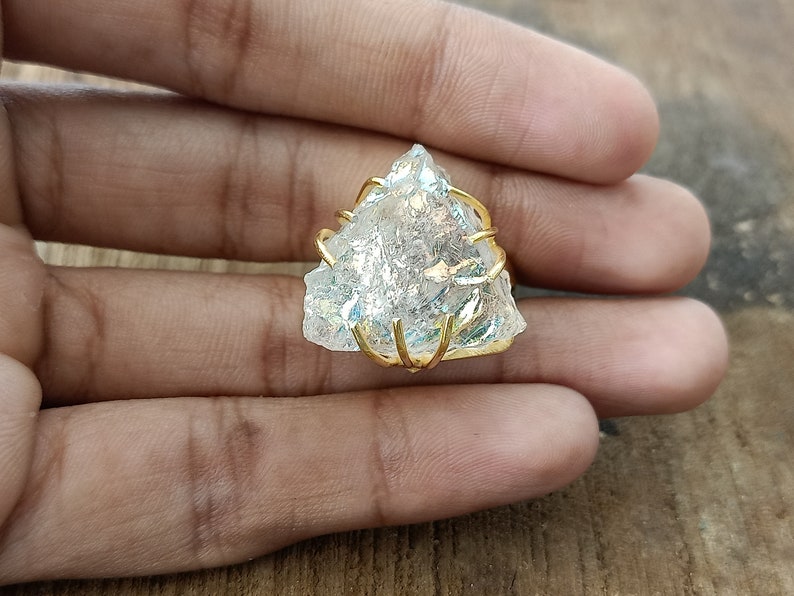 May include: A clear quartz crystal ring with a gold wire wrap. The crystal is a triangular shape and has a iridescent sheen.