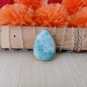 May include: A silver chain necklace with a teardrop-shaped pendant made of blue and white ocean jasper.