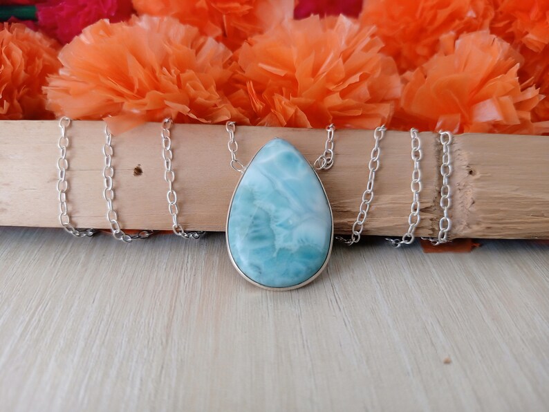 May include: A silver chain necklace with a teardrop-shaped pendant made of blue and white ocean jasper.