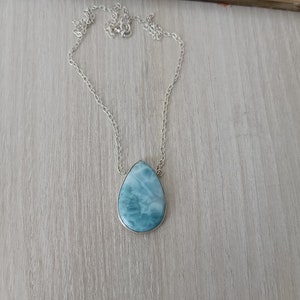 May include: A silver chain necklace with a teardrop-shaped blue and white gemstone pendant.