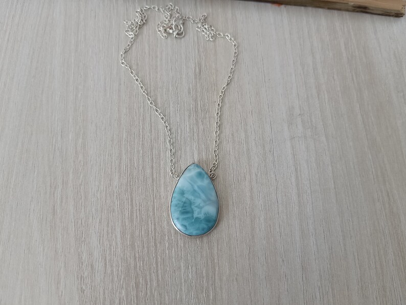 May include: A silver chain necklace with a teardrop-shaped blue and white gemstone pendant.
