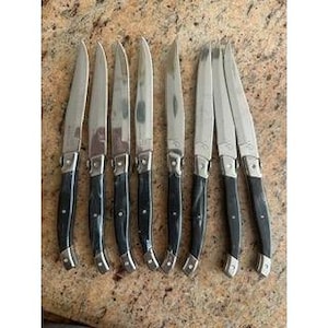May include: Set of eight steak knives with stainless steel blades and black handles. The knives have a classic design with a curved handle and a bolster where the blade meets the handle. The blades are approximately 9 inches long.