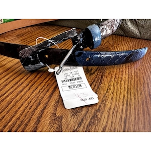 May include: A black and blue leather belt with a silver buckle. The belt has a Neiman Marcus price tag attached with the price of $65.00 and the size Medium.