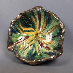 Puede incluir: Un cuenco de cer&aacute;mica pintado a mano con un dise&ntilde;o en forma de hoja. El cuenco presenta un borde dorado y un interior vibrante con tonos verdes, amarillos y rojos. La forma del cuenco es irregular, lo que aumenta su atractivo art&iacute;stico &uacute;nico.
