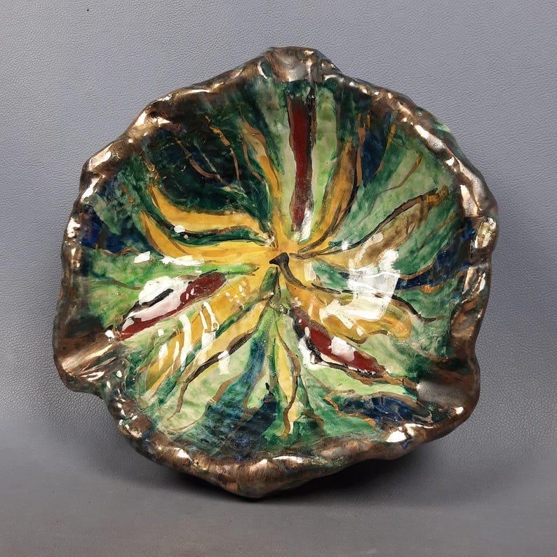 Puede incluir: Un cuenco de cer&aacute;mica pintado a mano con un dise&ntilde;o en forma de hoja. El cuenco presenta un borde dorado y un interior vibrante con tonos verdes, amarillos y rojos. La forma del cuenco es irregular, lo que aumenta su atractivo art&iacute;stico &uacute;nico.