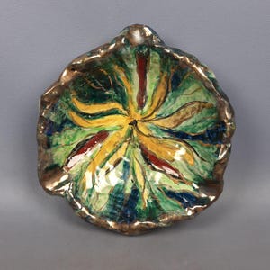 Puede incluir: Un plato de cer&aacute;mica pintado a mano con una forma org&aacute;nica &uacute;nica. El interior presenta un dise&ntilde;o vibrante con tonos amarillos, verdes, rojos y azules. El borde est&aacute; acentuado con un acabado dorado met&aacute;lico, agregando un toque de elegancia a esta pieza decorativa.