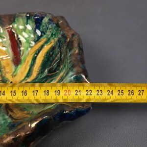 Puede incluir: Un plato decorativo de cer&aacute;mica colorida con una superficie texturizada. Presenta una mezcla de tonos verdes, amarillos, rojos y azules. Una cinta m&eacute;trica amarilla se coloca sobre el plato, mostrando una longitud de aproximadamente 35,5 a 68,5 cm.
