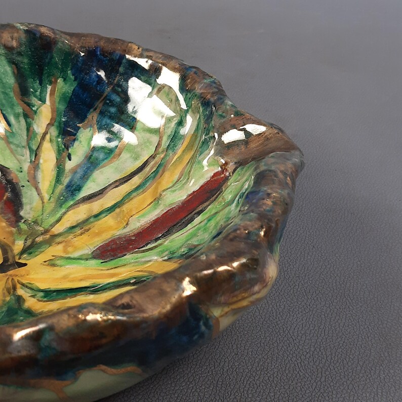 Puede incluir: Un cuenco de cer&aacute;mica hecho a mano con una forma org&aacute;nica &uacute;nica. El cuenco presenta un dise&ntilde;o abstracto vibrante con pinceladas verdes, amarillas, azules y rojas. El borde es de color marr&oacute;n oscuro. Este cuenco decorativo es ideal para servir o exhibir.