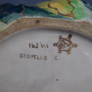 Puede incluir: Primer plano del interior de un cuenco de cer&aacute;mica con dise&ntilde;os florales pintados en azul, verde y amarillo. El borde del cuenco tiene una textura rugosa y sin esmaltar. La base es blanca con el texto "162 bis GROPELLO C." y un emblema dorado.