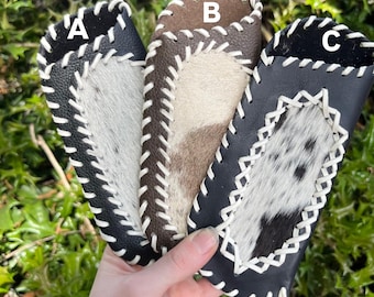 Op de afbeelding: Drie leren telefoonhoesjes met witte stiksels en een koehuidpatroon. De hoesjes zijn gemarkeerd met A, B en C.
