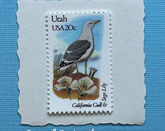 May include: A vintage 20-cent postage stamp featuring a California Gull and Sego Lily, with the text Utah USA 20c and Sego Lily California Gull & printed on the front. The stamp is mounted on a white scalloped-edge paper backing.