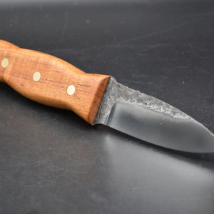 May include: A small, handmade knife with a wooden handle and a dark metal blade. The handle has three brass accents.