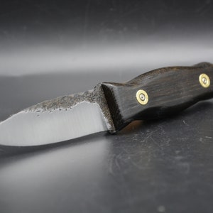Puede incluir: Un cuchillo pequeño con una hoja lisa ligeramente curvada y un mango de madera negro. El mango tiene dos remaches de latón.