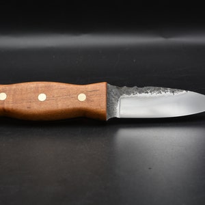 May include: A small, handmade knife with a wooden handle and brass accents. The blade is slightly curved and has a textured finish.