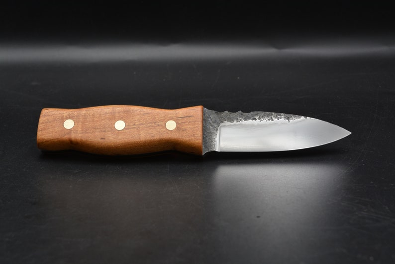 May include: A small, handmade knife with a wooden handle and brass accents. The blade is slightly curved and has a textured finish.