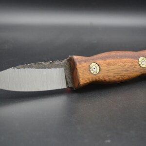 Puede incluir: Un pequeño cuchillo hecho a mano con mango de madera y hoja de metal. El mango está decorado con dos casquillos de bala de latón.