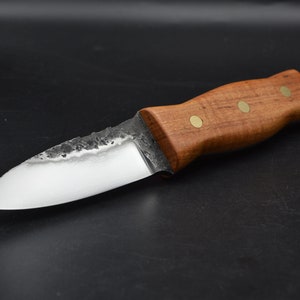 May include: A small, handmade knife with a wooden handle and brass accents. The blade is made of steel and has a slightly curved shape.