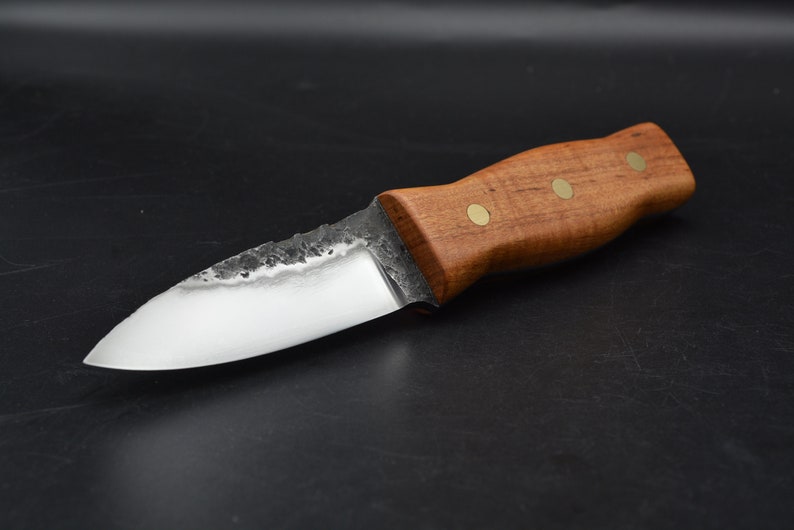 May include: A small, handmade knife with a wooden handle and brass accents. The blade is made of steel and has a slightly curved shape.