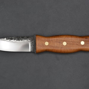 May include: A small, sharp knife with a brown wooden handle and brass accents. The blade is made of steel and has a slightly curved edge.