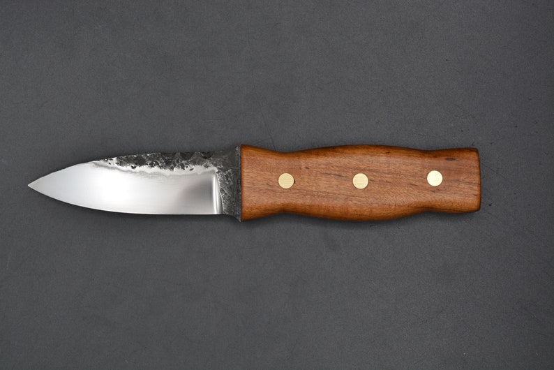 May include: A small, sharp knife with a brown wooden handle and brass accents. The blade is made of steel and has a slightly curved edge.