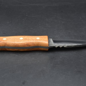 May include: A small, black, serrated knife with a wooden handle. The handle has a dark brown stain and three white dots.