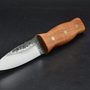 May include: A small, handmade knife with a wooden handle and brass accents. The blade is made of steel and has a slightly curved edge.