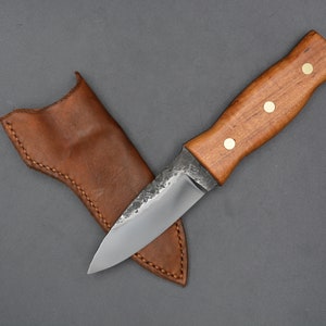 May include: A small, handmade knife with a brown wooden handle and a leather sheath. The blade is made of steel and has a slight curve.