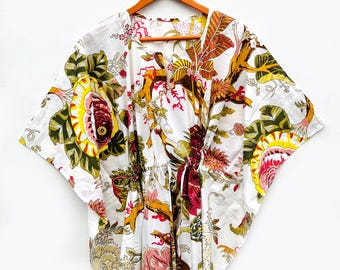 May include: White cotton kaftan with a vibrant floral print in shades of yellow, green, red, and brown. The kaftan features a drawstring waist and wide sleeves, hanging on a wooden hanger.
